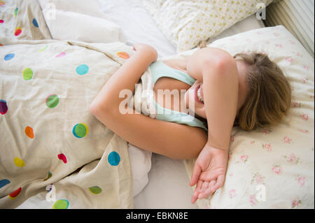 La ragazza (12-13) che giace nel letto che copre il volto Foto Stock