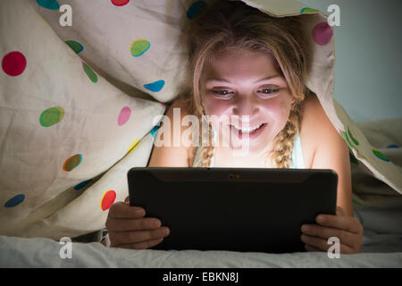 La ragazza (12-13) utilizzando tablet a letto Foto Stock