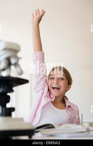 La ragazza (12-13) alzando la mano per rispondere alla domanda a scuola Foto Stock