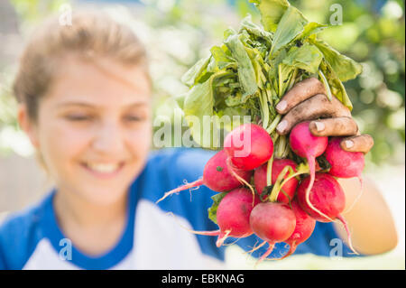 La ragazza (12-13) che mostra un mazzetto di ravanello Foto Stock