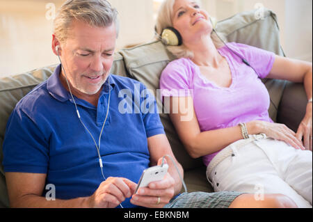 Ritratto di giovane seduto sul divano ascoltando la musica sulle cuffie Foto Stock