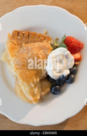 Close-up shot della porzione di fetta di torta di mele con frutti di bosco freschi e crema sulla piastra bianca Foto Stock