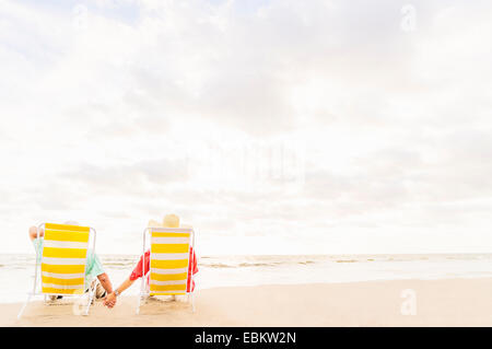 Stati Uniti d'America, Florida, Giove, vista posteriore del giovane seduto in sedie a sdraio sulla spiaggia Foto Stock