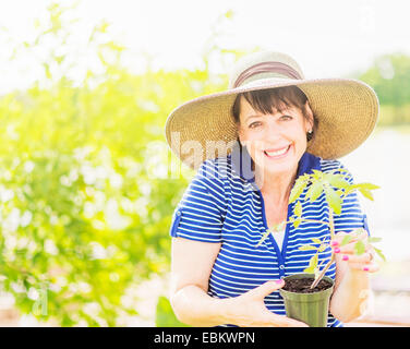 Ritratto di donna sorridente azienda pianta in vaso in giardino Foto Stock