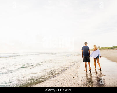 Stati Uniti d'America, Florida, Giove, coppia giovane camminando lungo la linea surf di spiaggia sabbiosa, tenendo le mani Foto Stock