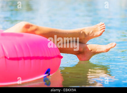 Tagliate il colpo di gambe della giovane donna galleggiante sul rosa anello nuotare Foto Stock