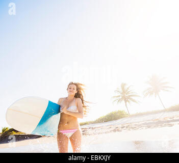 Stati Uniti d'America, Florida, Giove, giovane donna in esecuzione in surf che trasportano le tavole da surf Foto Stock