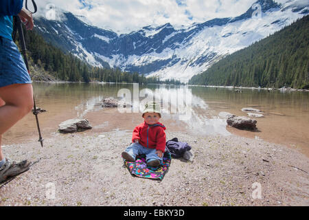 Stati Uniti d'America, Montana, il Glacier National Park, Lago di valanghe, ragazzo (4-5) seduto sul lungolago Foto Stock
