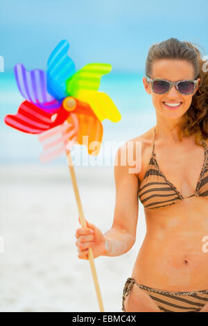 Sorridente giovane donna che mostra girandola colorata toy sulla spiaggia Foto Stock