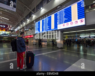 L'uomo con la valigia di fronte alla pianificazione del volo pensione all'Aeroporto Internazionale Capital di Pechino, Cina Foto Stock