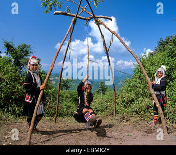 Cerimonia di oscillazione, un harvest festival rituale, tre giovani ragazze Akha ad una oscillazione in costume tradizionale e copricapo Foto Stock