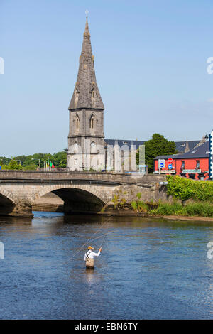 Salmone atlantico, ouananiche, lago di salmone atlantico, senza sbocco sul mare salmone, la Sebago salmone (Salmo salar), pescatore di salmone nel fiume con la canna da mosca a fronte di un ponte e una chiesa, Irlanda, Moy River, Ballina Foto Stock