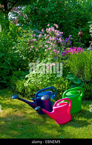 Tre impianti di irrigazione in plastica lattine in piedi a fianco a fianco su un giardino prato in un letto di fiori, Germania Foto Stock