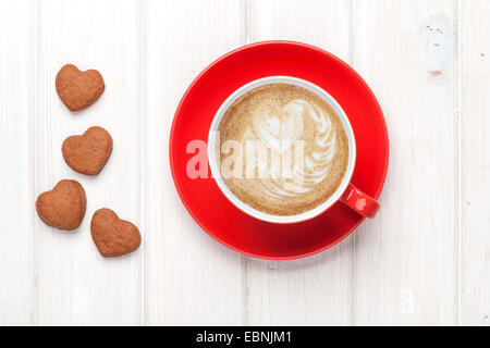 Il giorno di San Valentino a forma di cuore e i cookie red tazza di caffè. Vista da sopra in bianco tavolo in legno Foto Stock