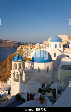 Ia, Santorini, Egeo Meridionale, Grecia. Tipico blu-cupola chiese aggrappati alla collina sopra la caldera, sunrise. Foto Stock