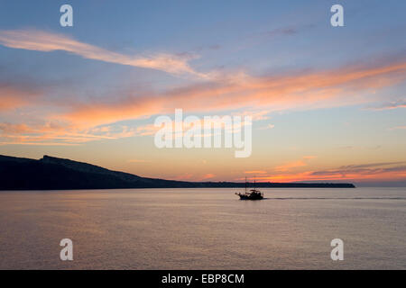 Ia, Santorini, Egeo Meridionale, Grecia. Nuvole rosa sopra l'isola di Thirasia, crepuscolo, imbarcazioni da diporto che passa. Foto Stock