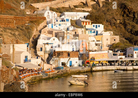 Ia, Santorini, Egeo Meridionale, Grecia. Waterfront edifici di Ammoudi baia illuminata dal sole al tramonto. Foto Stock