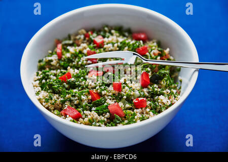 Tabulé insalata in una ciotola bianco su uno sfondo blu scuro con argento cucchiaio e una forcella Foto Stock