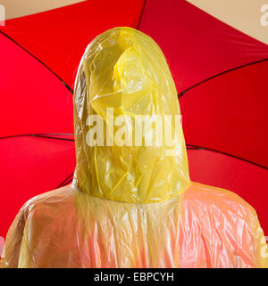 Donna che indossa il poncho giallo azienda Ombrellone rosso Foto Stock