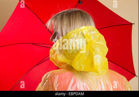 Donna che indossa il poncho giallo azienda Ombrellone rosso Foto Stock