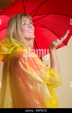 Donna che indossa il poncho giallo azienda Ombrellone rosso Foto Stock