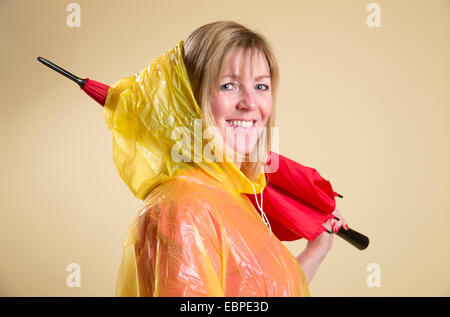 Donna che indossa il poncho giallo azienda Ombrellone rosso Foto Stock