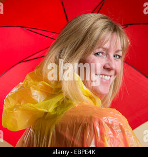 Donna che indossa il poncho giallo azienda Ombrellone rosso Foto Stock