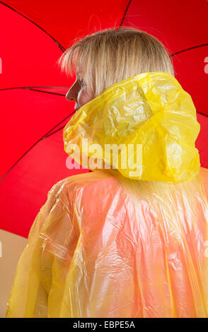 Donna che indossa il poncho giallo azienda Ombrellone rosso Foto Stock