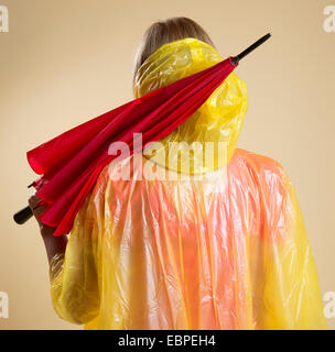 Donna che indossa il poncho giallo azienda Ombrellone rosso Foto Stock