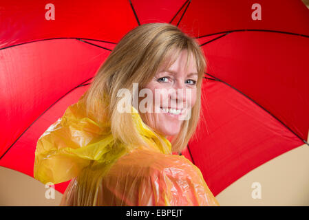 Donna che indossa il poncho giallo azienda Ombrellone rosso Foto Stock