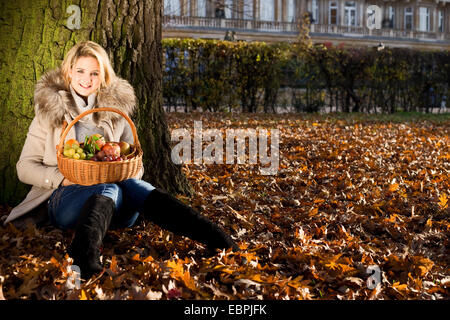 Giovane donna seduta in un parco con un cesto di frutta. Foto Stock