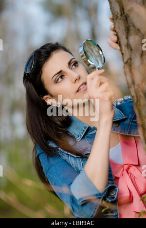 Donna che guarda la corteccia di albero attraverso una lente di ingrandimento Foto Stock