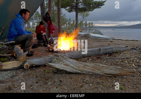 Giovane seduto presso il fuoco a Isteren lungolago, Norvegia, Hedmark Fylke, Naturreservat Isteren Foto Stock