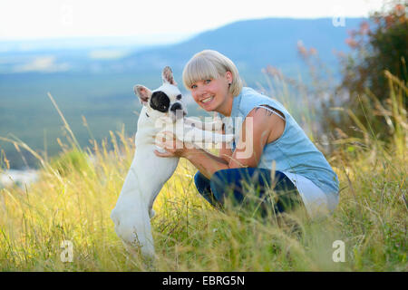 Bulldog francese (Canis lupus f. familiaris), donna e cane abbracciando in un prato, Germania Foto Stock