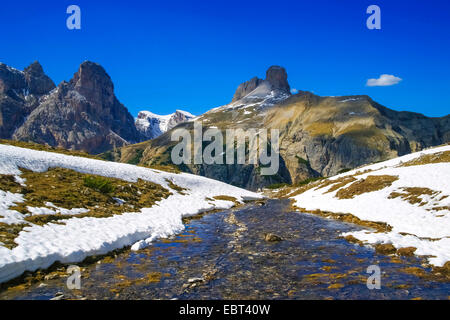 Vista da Tre Cime di Lavaredo al mountain creek e campi di neve nel paesaggio di montagna, Schwabenalpenkopf e Gwengalpenjoch in background, Italia, Alto Adige, Dolomiti Foto Stock