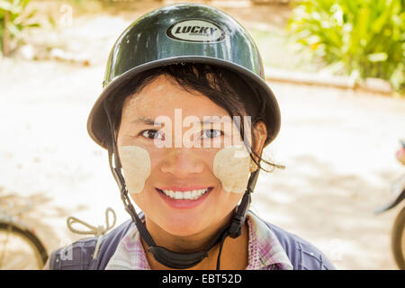 Una giovane donna che indossa un casco in moto con pasta Thanaka dipinta sul suo volto. Foto Stock