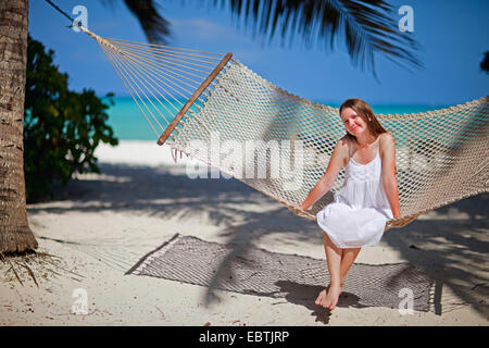 Una giovane donna attraente seduta in una amaca in spiaggia tropicale Foto Stock