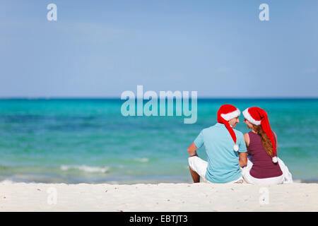 Un giovane in amore seduta con cappelli di Babbo Natale a Sandy Beach Foto Stock