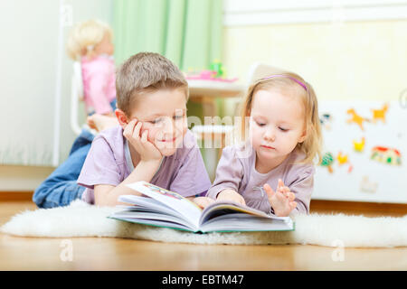 Fratello e Sorella sdraiato sul pavimento nel loro nido la lettura di un libro insieme Foto Stock