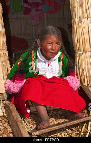 Uro ragazza seduta all' entrata di un capanno sul galleggiante Isole Uros, Perù Lago Titicaca Foto Stock