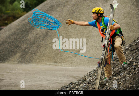 Sciatore freeride in piedi sul pendio roccioso e gettando una fune di arrampicata Foto Stock