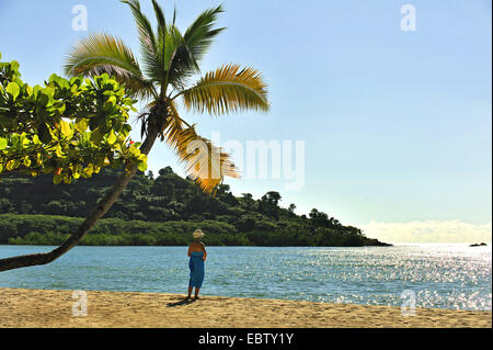 Donna in piedi sotto il palm tree a Sandy Beach, Madagascar, Nosy be Foto Stock