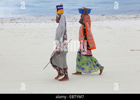 Le donne trasportano contenitori sui suoi capi sulla spiaggia sabbiosa, Tanzania, Sansibar Foto Stock