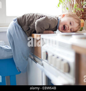 Little Boy ridere mentre si arrampica sul bancone della cucina Foto Stock