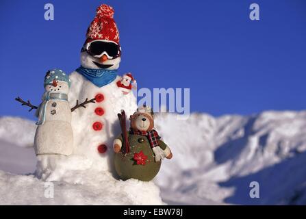 Pupazzo di neve con bobble cappello e occhiali da sci di fronte coperta di neve la gamma della montagna e cielo blu, Francia Foto Stock