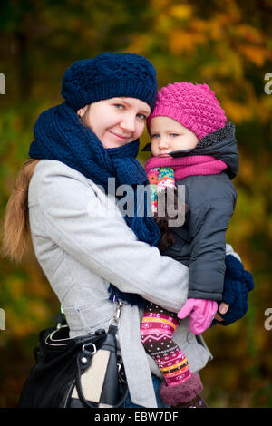 Madre cullano la figlia sia in abiti caldi con cappello di lana e sciarpa Foto Stock