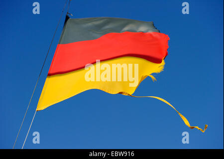 Nazionale tedesco di bandiera strappata nel vento ists sventolando nella parte anteriore del cielo blu Foto Stock