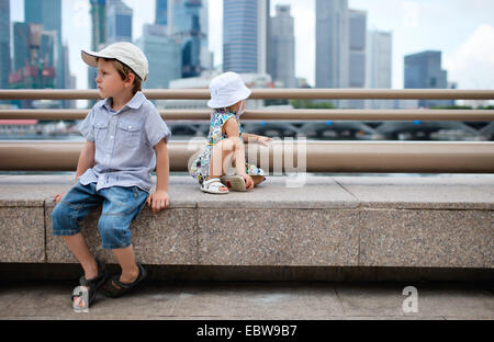 Due piccoli bambini seduti nel centro città, Singapore, Singapore Foto Stock