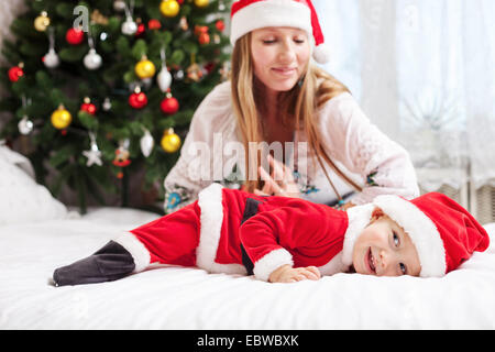 Giovane madre giocando con il bambino vestito in costume di Santa Foto Stock