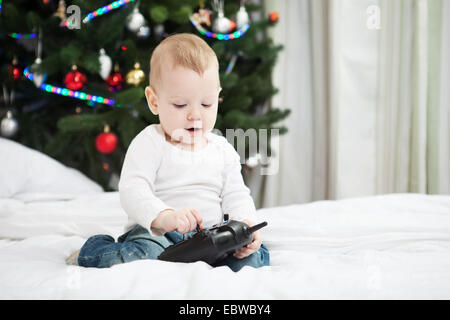 Il Toddler boy azienda RC controller mentre seduto sul letto di casa al tempo di Natale Foto Stock